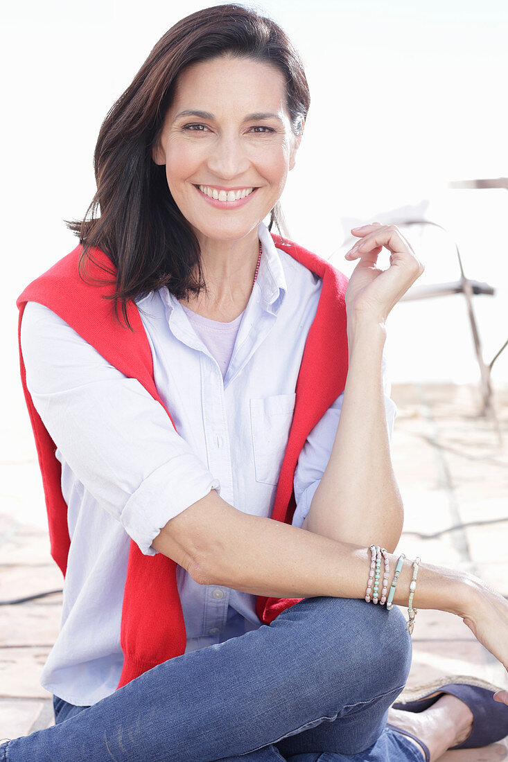 A brunette woman wearing a light shirt with a red jumper over her shoulders