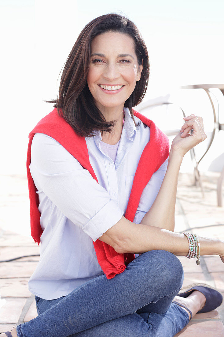 A brunette woman wearing a light shirt with a red jumper over her shoulders