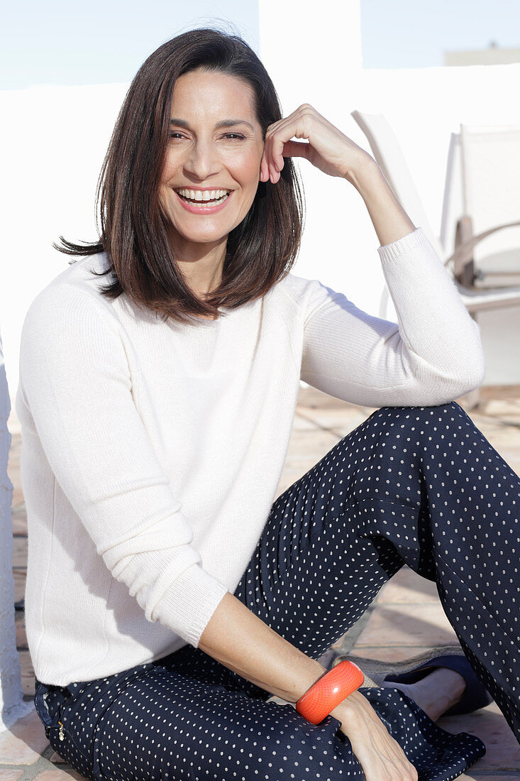 A brunette woman wearing a white jumper and polka dot trousers