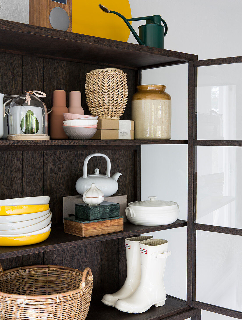 Baskets, crockery, wellington boots and ornaments in dark display cabinet