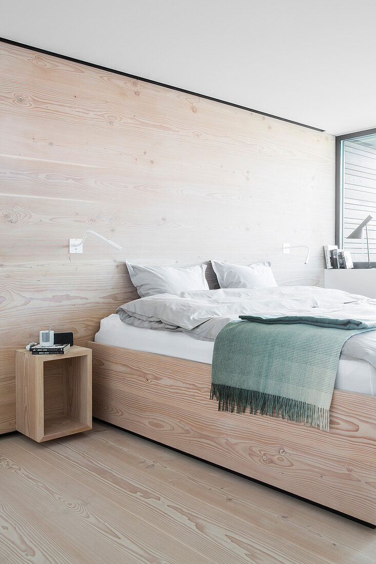 Bed in bedroom with pale wooden floor and walls