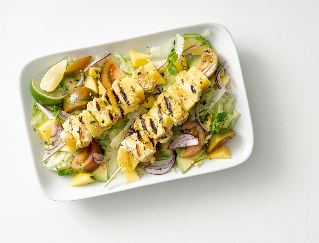 Grilled chicken and pineapple skewers on a mixed leaf salad