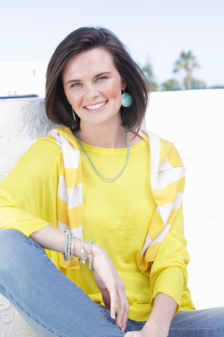 A young woman wearing a long-sleeved yellow top and jeans with a jumper over her shoulders