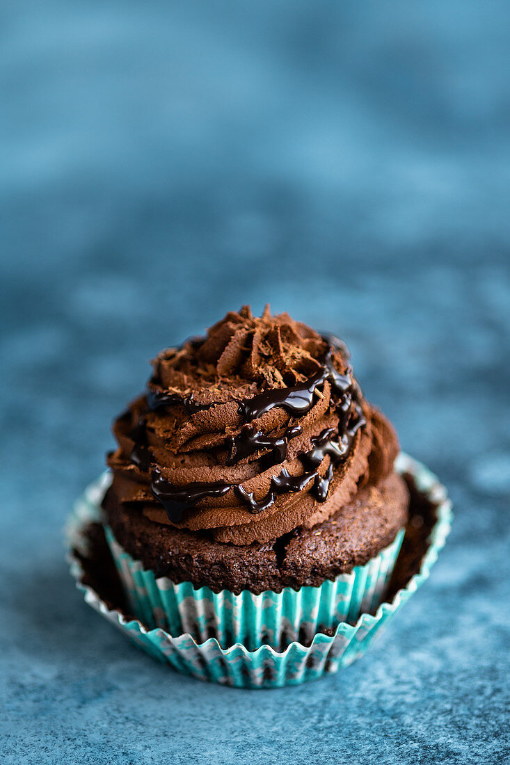 A vegan chocolate cupcake with frosting and chocolate sauce