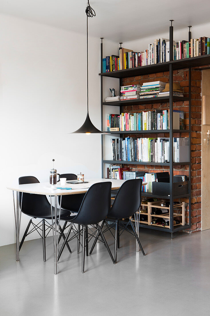 Black shell chairs at dining table and bookcase against brick wall