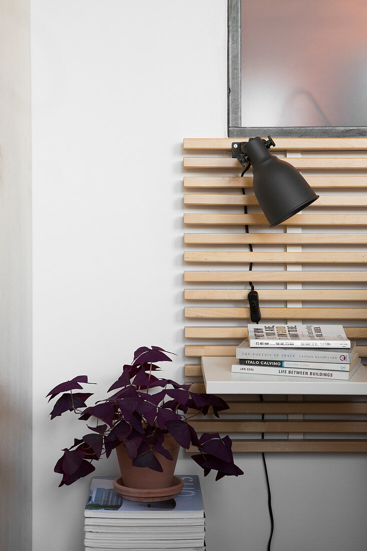 Potted red oxalis on stacked books next to bed headboard with integrated shelf