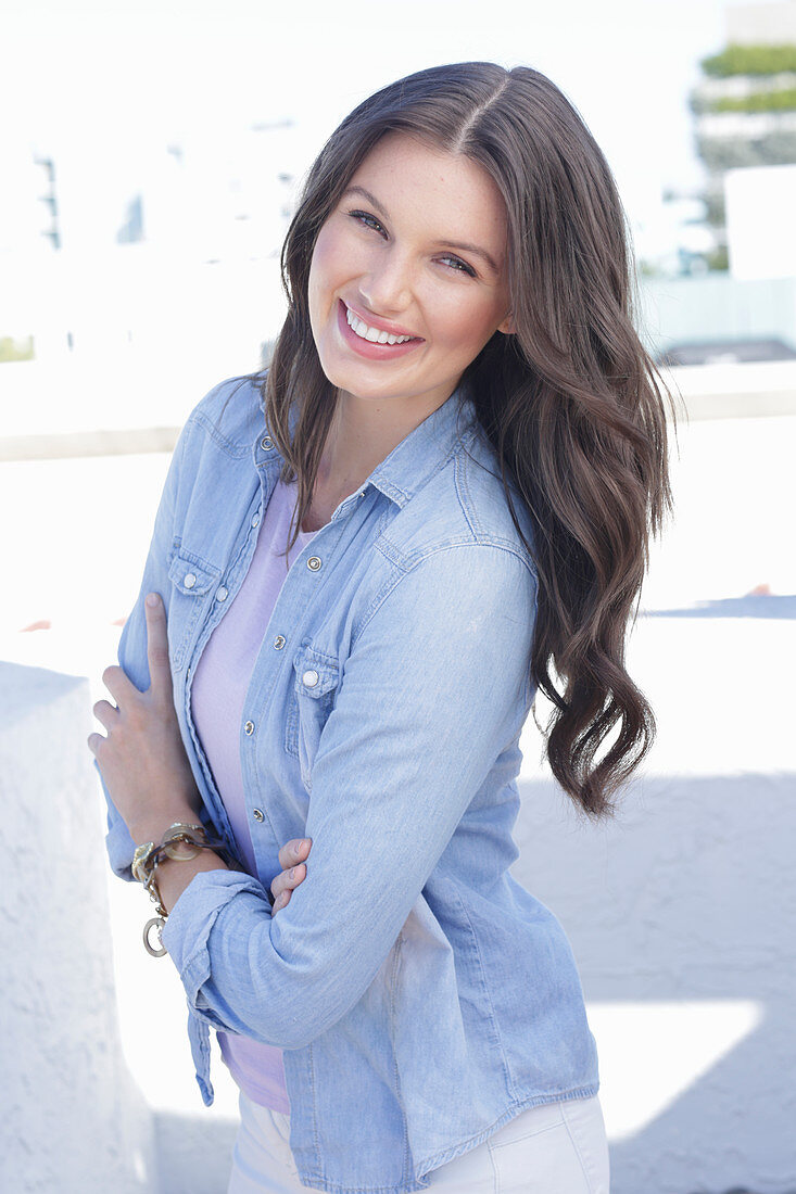 A young woman wearing a purple t-shirt, a denim shirt and white trousers