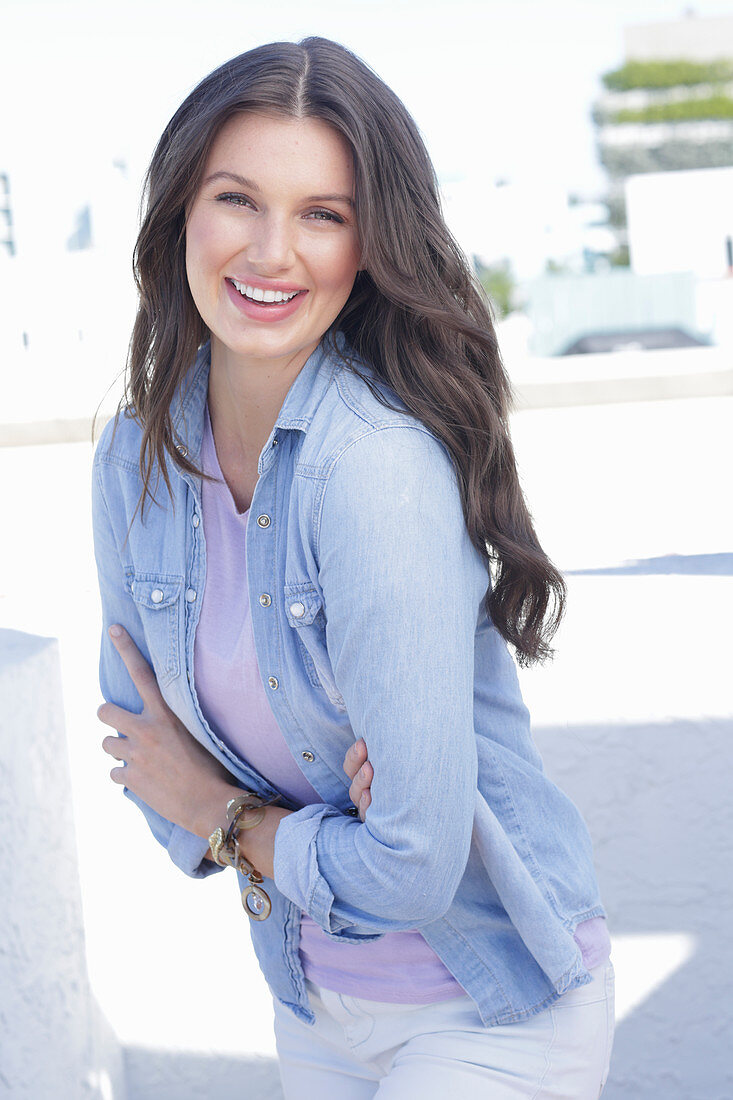 A young woman wearing a purple t-shirt, a denim shirt and white trousers