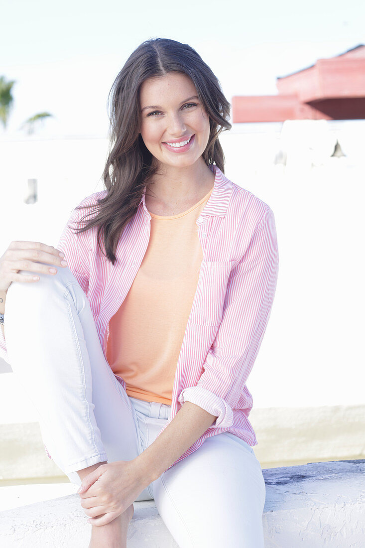 A young woman wearing an apricot top, a pink striped shirt and white trousers