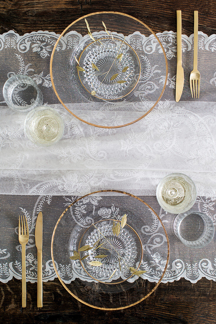 Table set with glass plates, golden cutlery and lace tablecloth