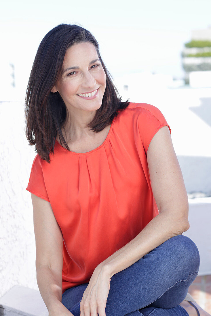 Reife, brünette Frau in roter Bluse und Jeans