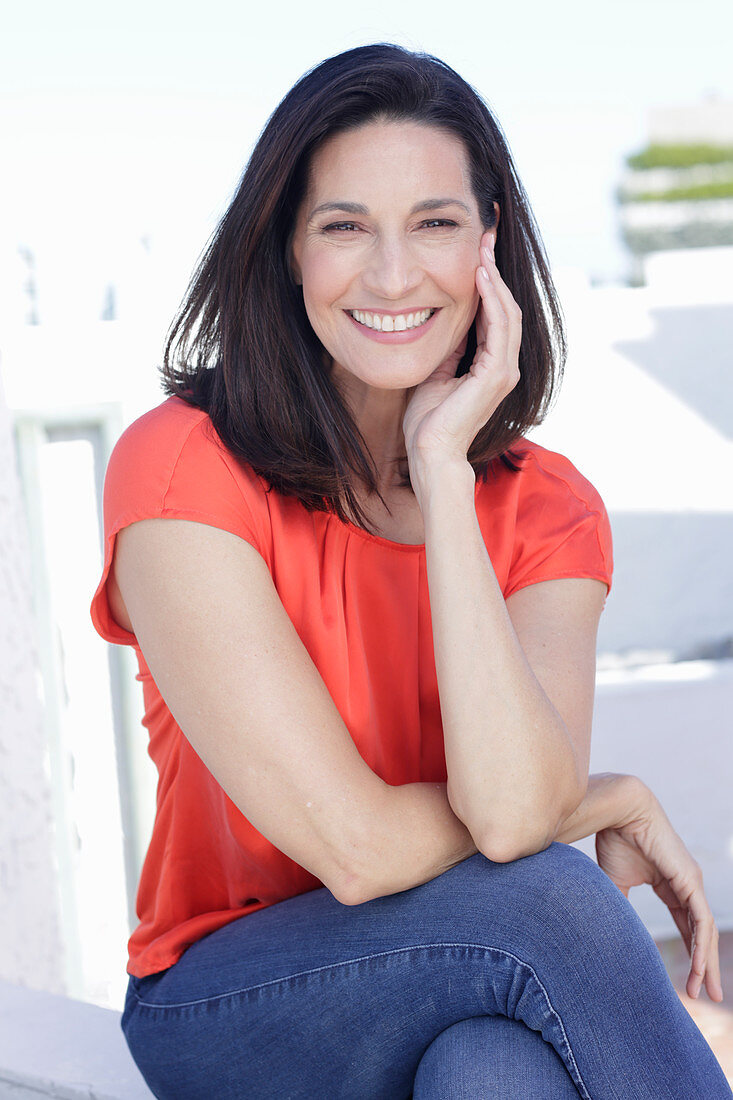 Reife, brünette Frau in roter Bluse und Jeans