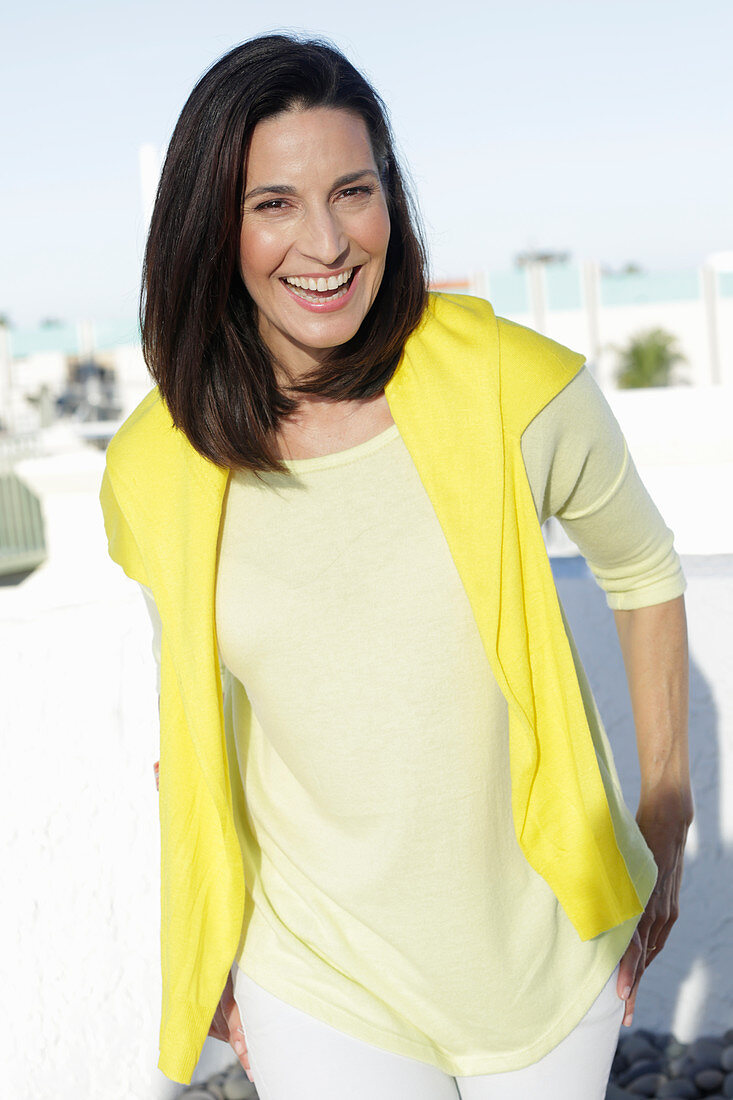 Reife, brünette Frau in gelbem Shirt mit Pulli über den Schultern