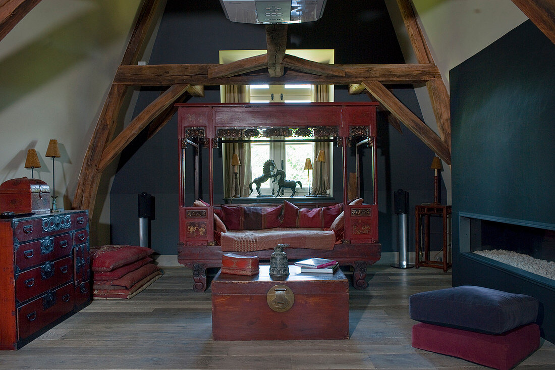 Antique wooden sofa and wooden trunk used as coffee table in attic room with wood-beamed ceiling