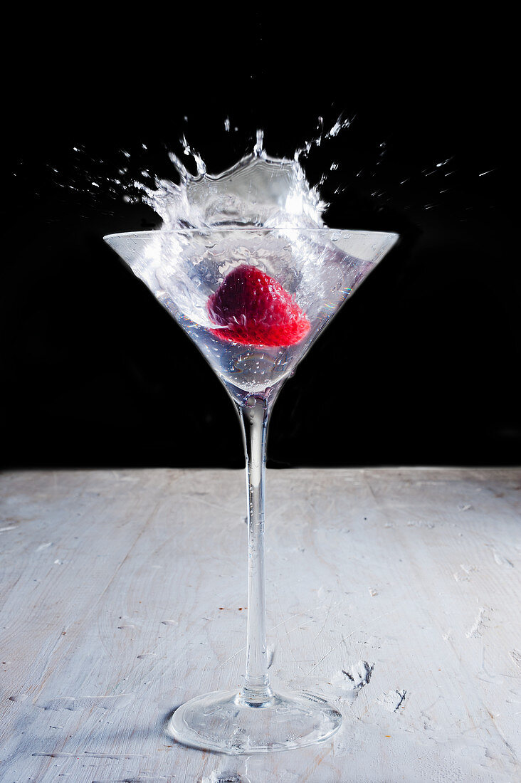A drink with with a strawberry and a splash against a black background