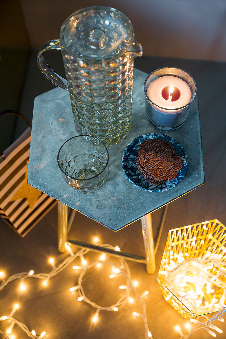 Glass jug and candle on side table with festive fairy lights below