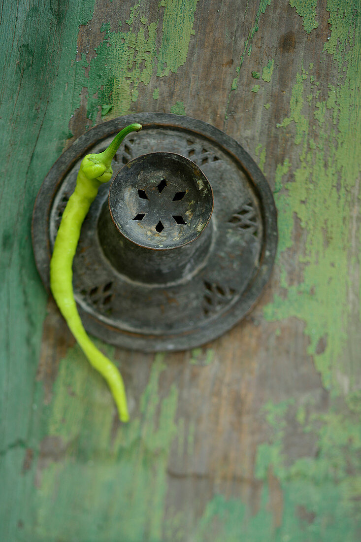 A green pepperoni on a green wooden surface