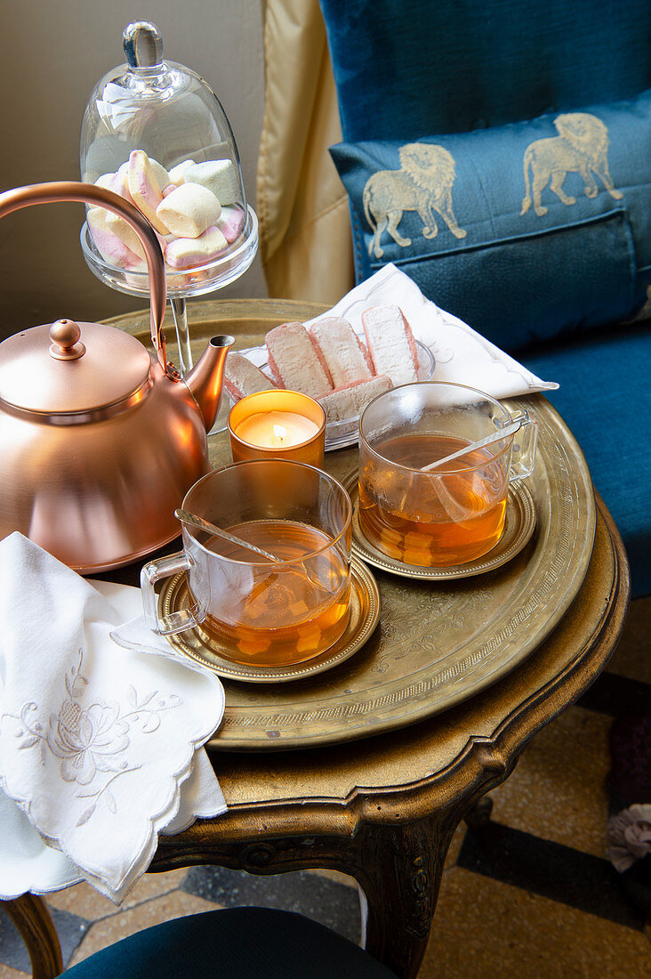 A copper pot, tea glasses and cake on a stylish side table