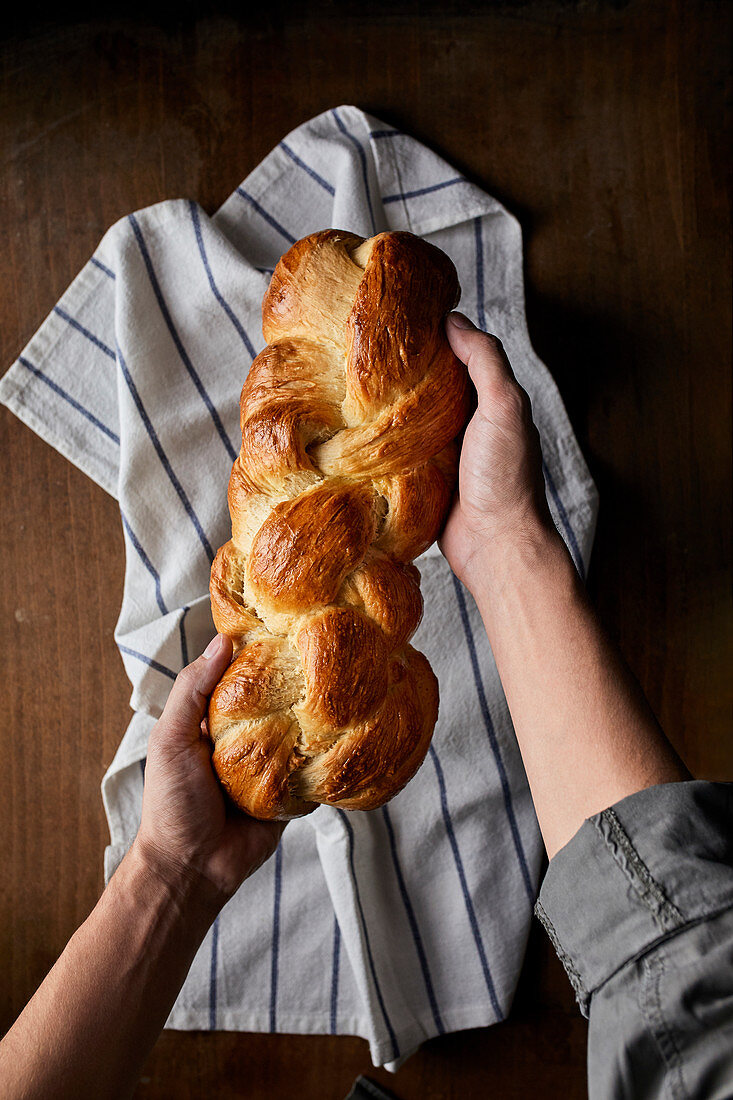 Hands holding a homemade loaf of braided bread