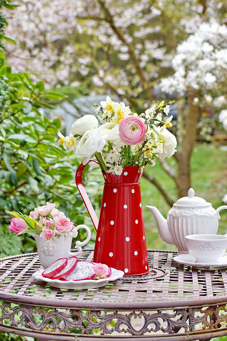 Spring bouquet with ranunculus, daffodils and blossom branches in a tin can, mini-bouquet of rose blossoms, and tulips in a creamer pitcher