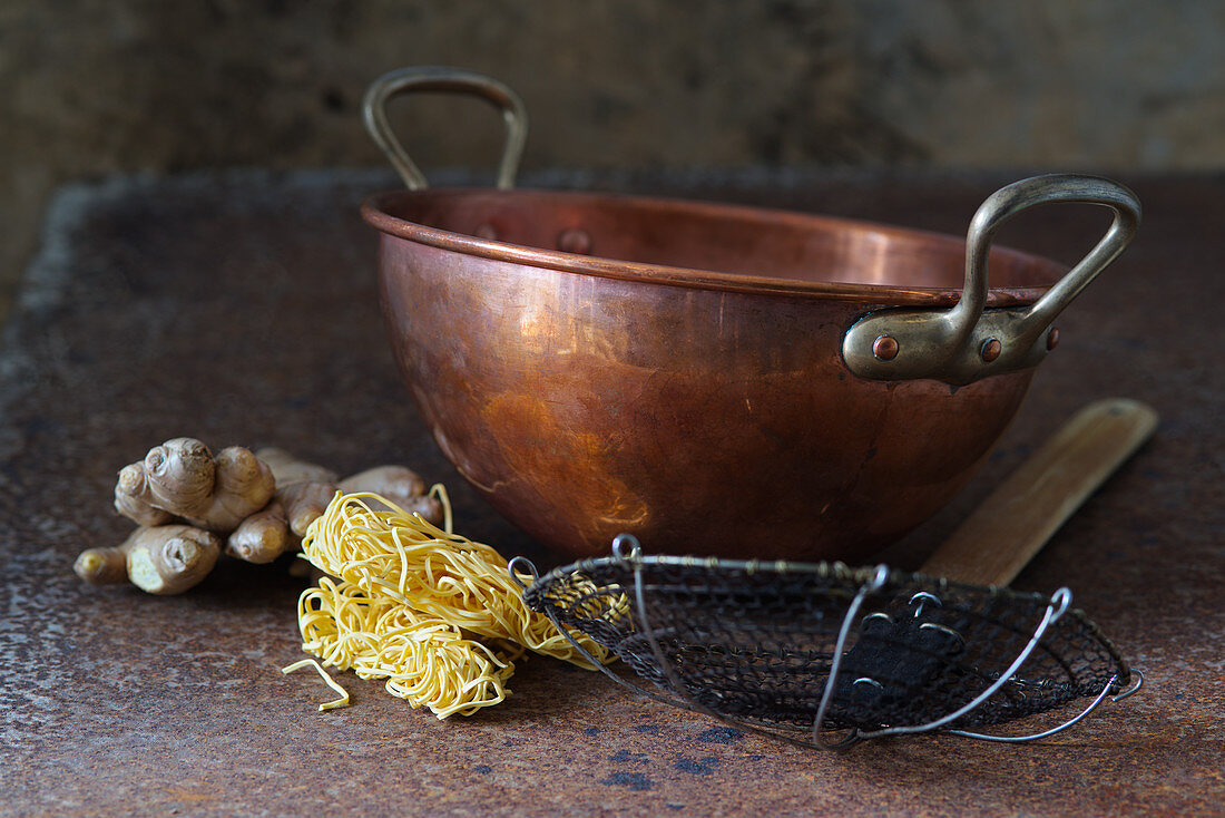 Asian still life with a copper bowl, sieve spoon, egg noodles and ginger