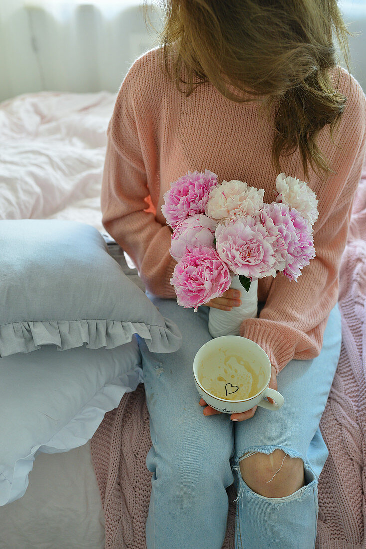 Woman is holding an empty coffee cup in her hands and a bouquet of peonies
