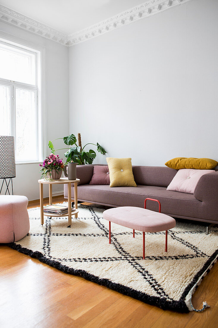 Sofa mit Kissen, Zimmerpflanze und Beistelltische auf hellem Teppich