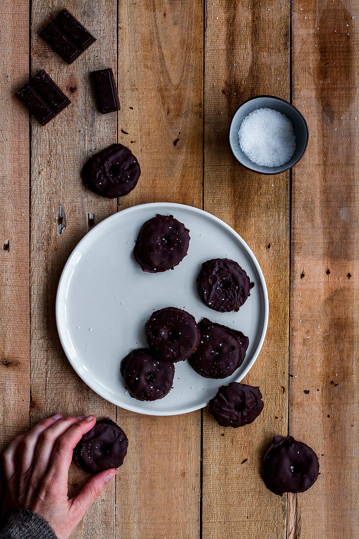 Hand grabbing cookies covered with chocolate syrup in white plate on wooden table