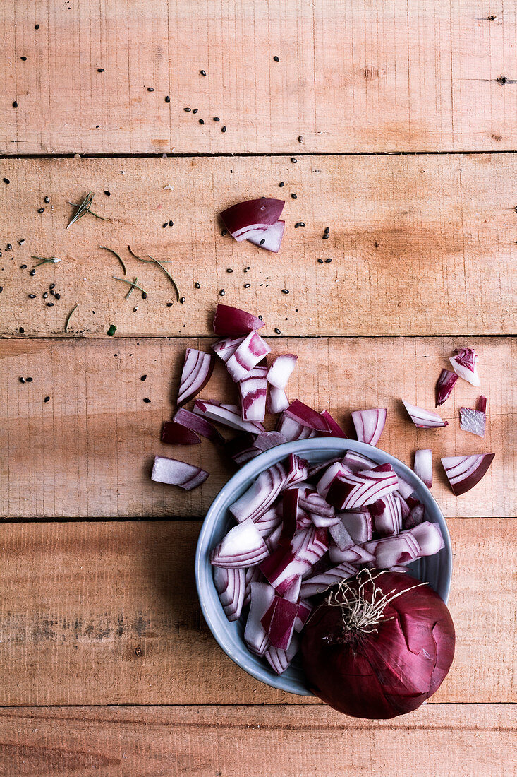 Raw chopped red onion in bowl and on rustic wooden table