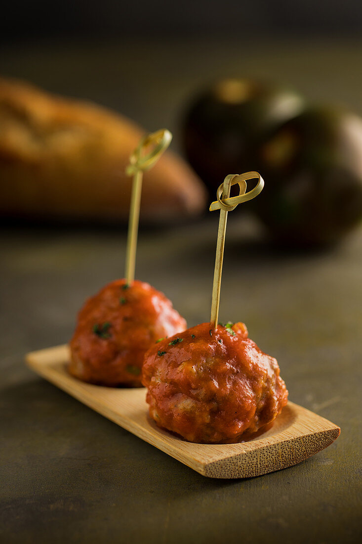 Meat balls with tomato sauce bonded with bamboo sticks on flat board on table