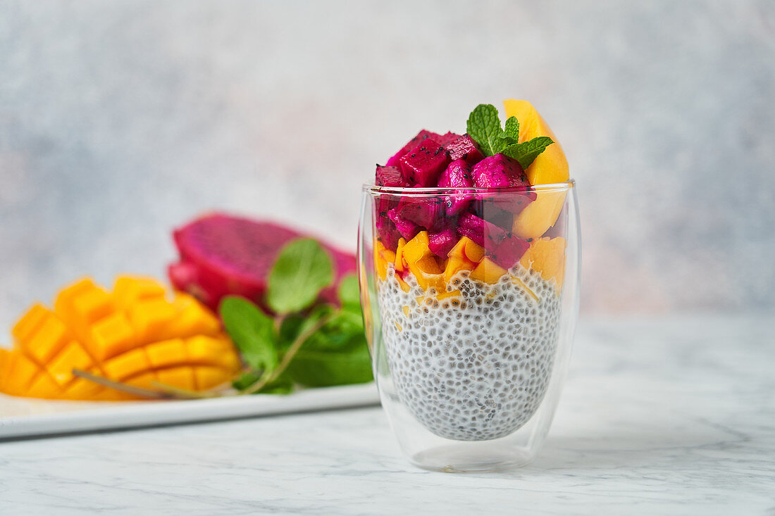 Chia pudding decorated with slices of mango red pitaya and fresh mint in glass
