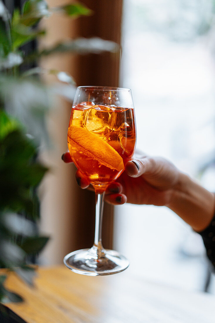 Woman holding alcohol cocktail with aperol and campari decorated with slices of orange