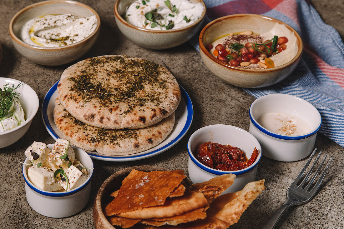 Served dishes of cheese, hummus and jerked meat with flatbread on gray table