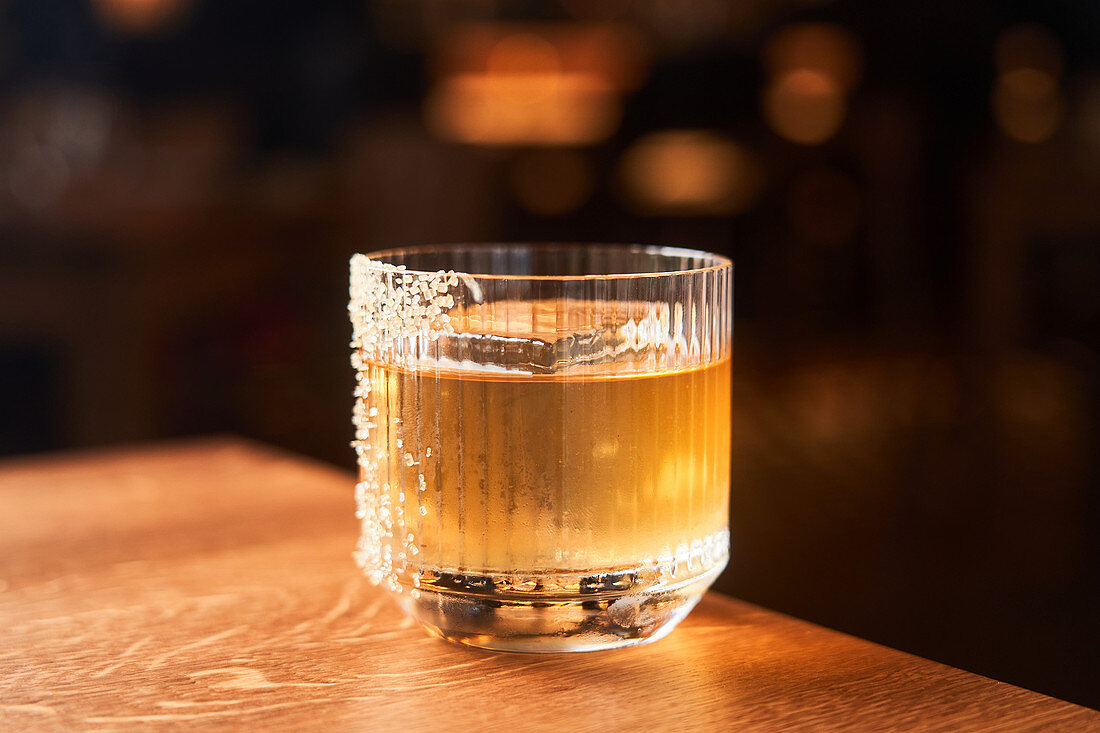 Amber whiskey cocktail with ice decorated with sugar placed on wooden counter