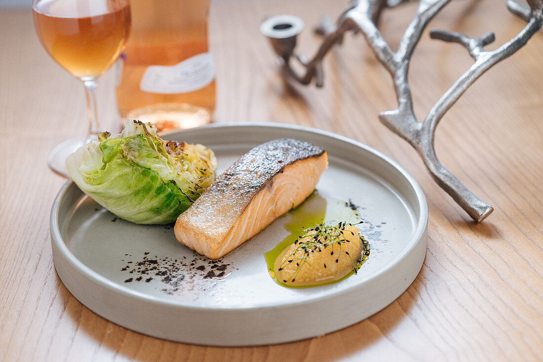 Steamed salmon served with grilled cabbage on white ceramic plate on wooden table