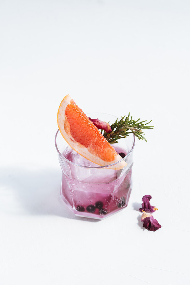 Cocktail mit Grapefruit, Rosmarin, getrockneten Blaubeeren, Trockenblüten und Eiswürfel