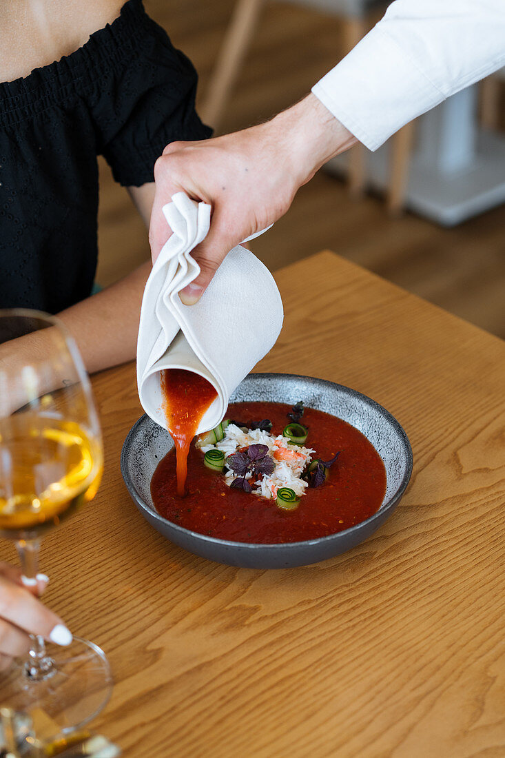 Waiter pouring tomato sauce into bowl with rice dish, vegetables and herbs