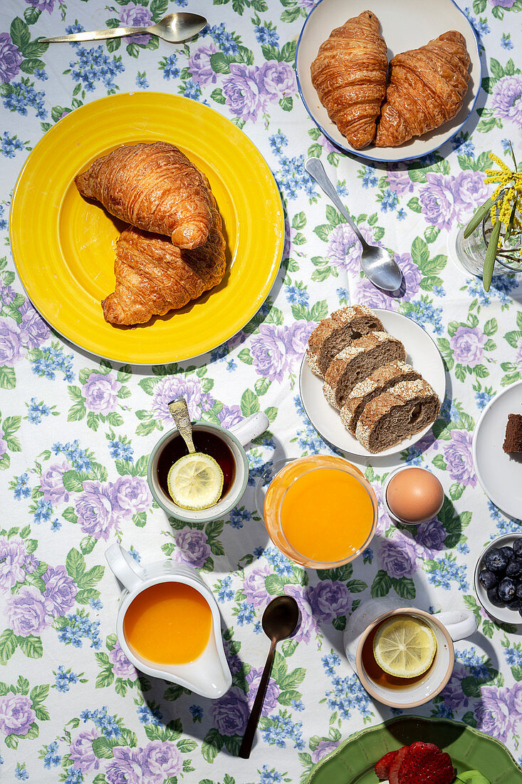 Breakfast with cooked eggs, cake, croissants, toast, tea and orange juice