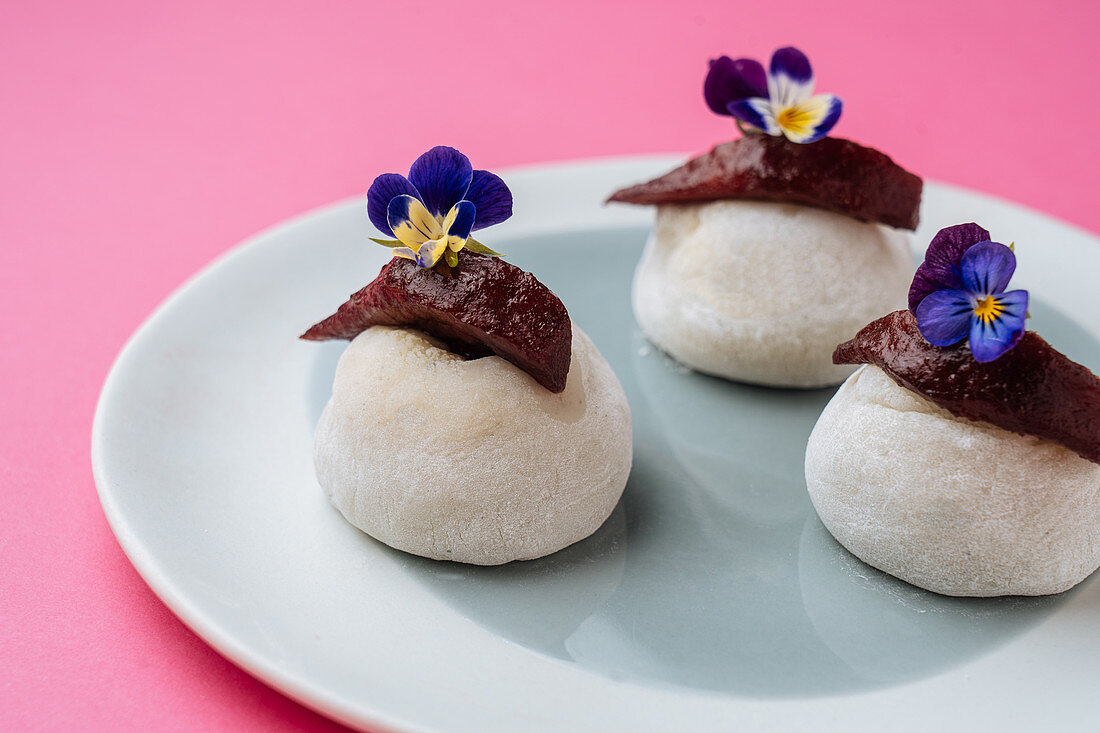 Rock shaped pastry with berry marmalade, flowers and placed on plate on pink background