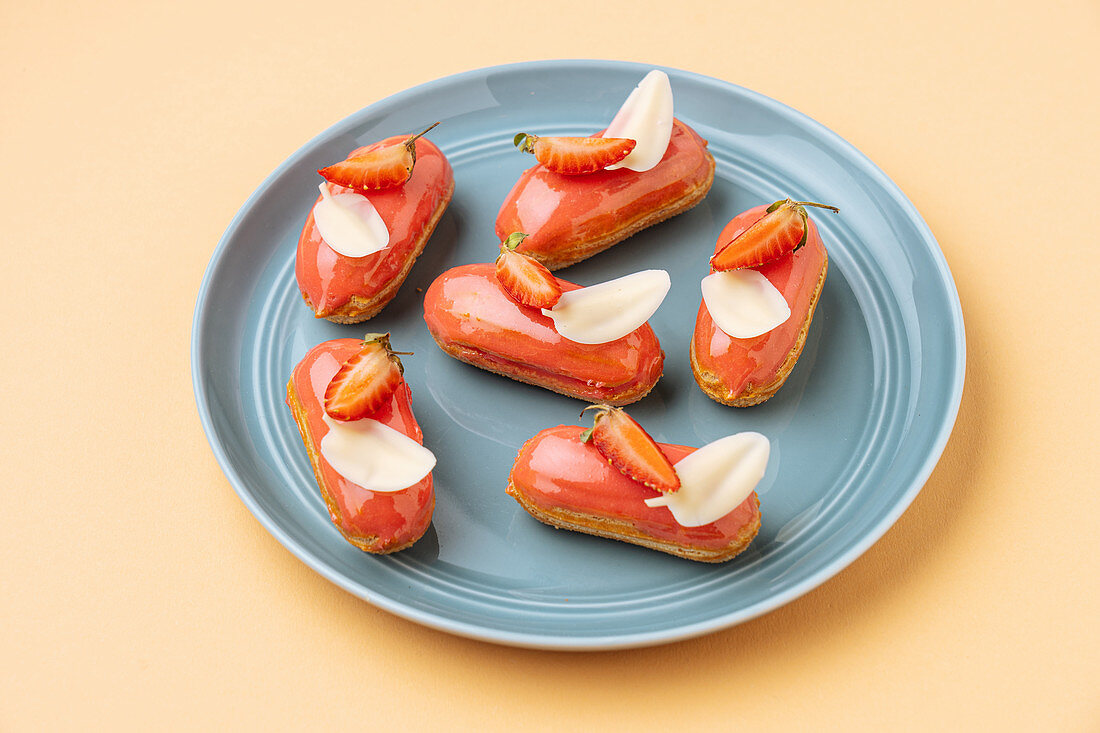 Eclairs with strawberry icing and white chocolate leaves placed on beige background