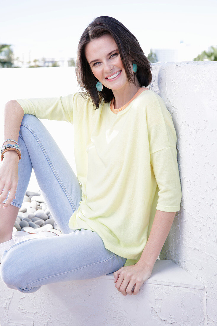 A young woman wearing an apricot top, a yellow jumper and jeans