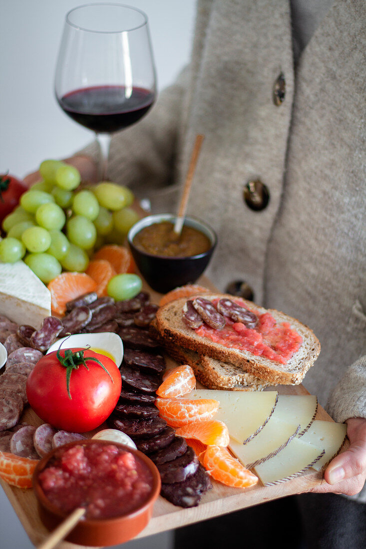 Waiter carrying wooden tray with sliced of meat vegetables fruits and glass of red wine