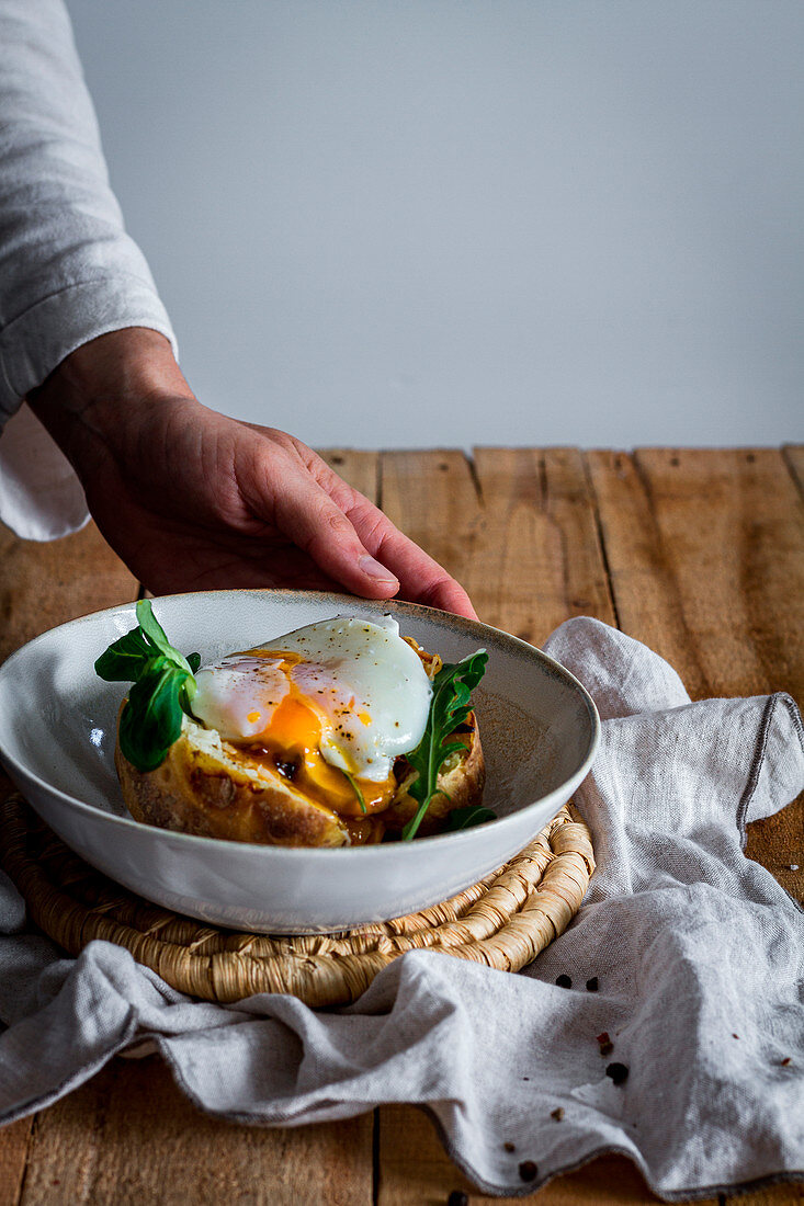 Hand holding dish with fried egg on potato with fried mushrooms, grated cheese and herbs