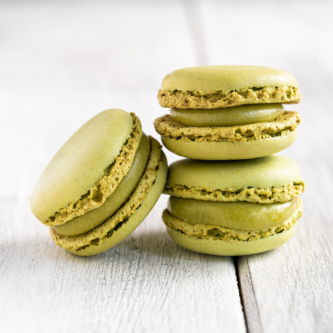Green macaroons stacked in pile against wooden white surface