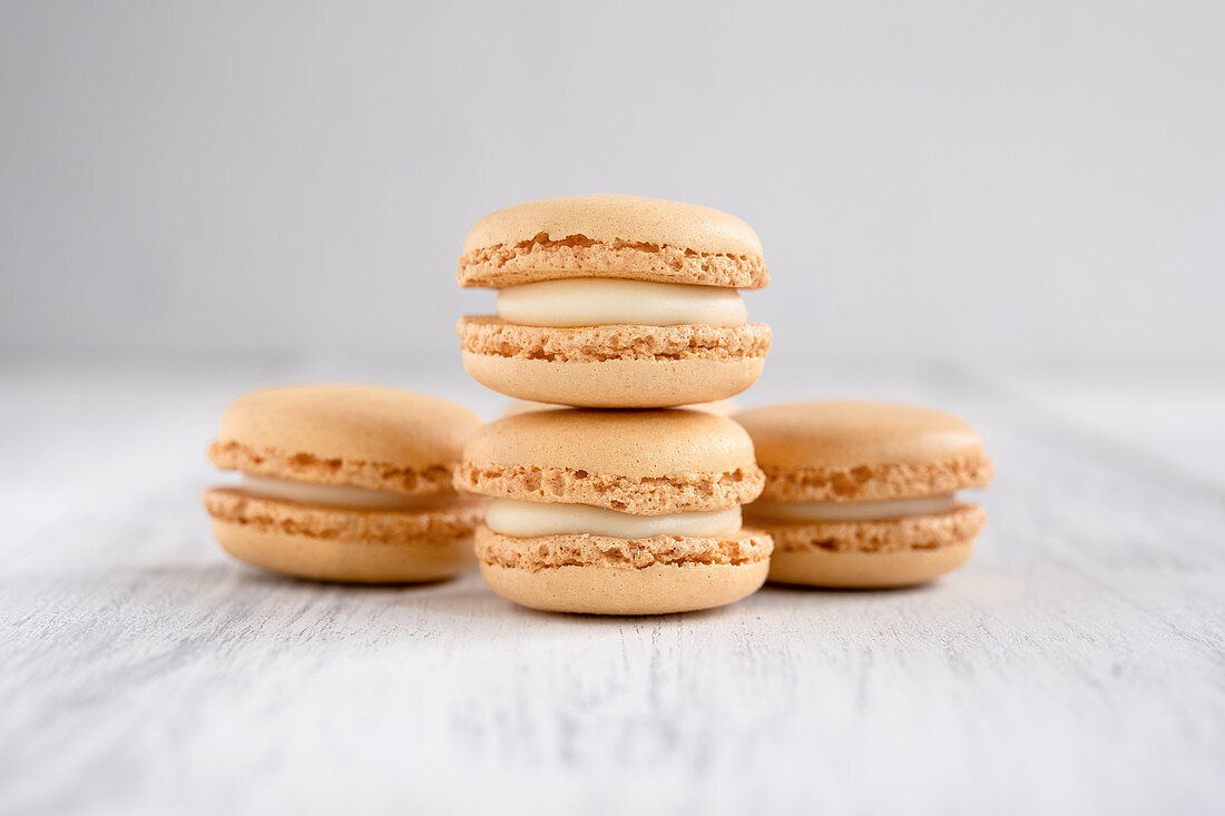Orange macaroons stacked in pile against wooden white surface