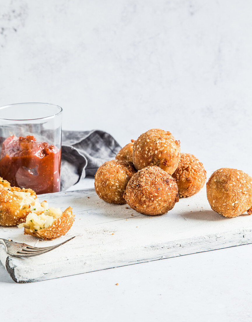 Arancini balls served with with tomato relish, on white wooden board