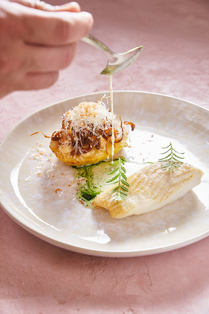 Chef with spoon adding cream sauce to yummy fish dish with herb