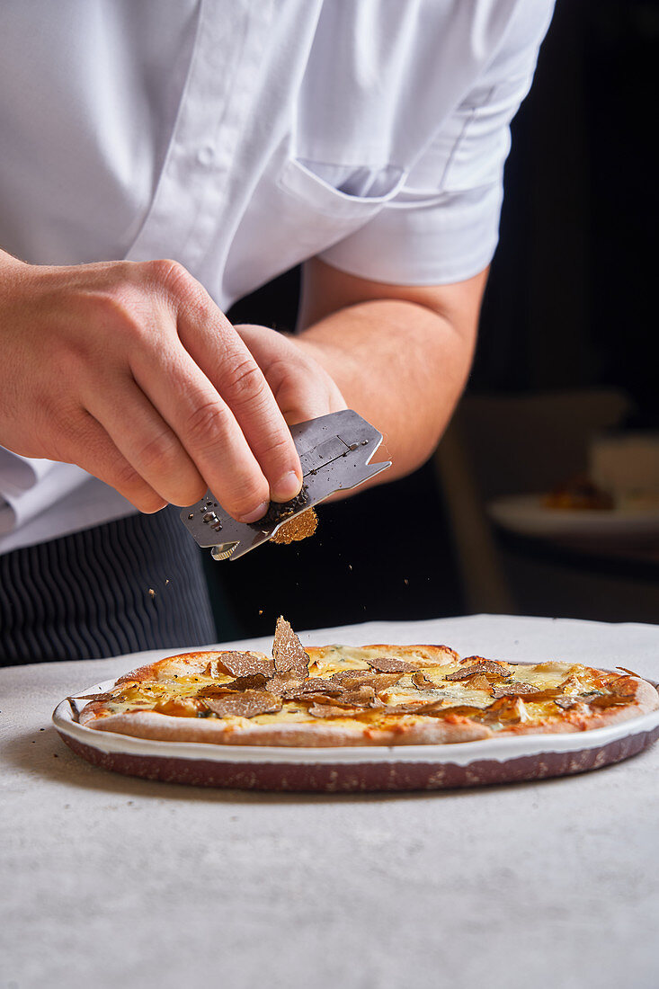 Cook slicing fresh truffle on tasty pizza