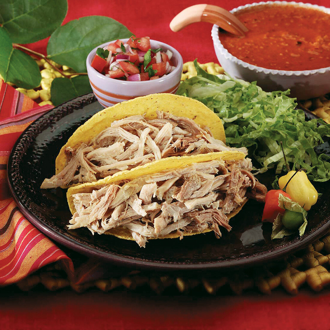 Pork carnitas in a crispy corn taco shell garnished with tomatillo, peppers, shredded lettuce and tomato salsa