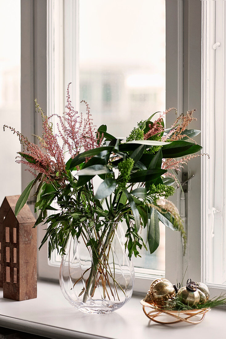 Wintry bouquet of leaves and grasses in glass vase on windowsill